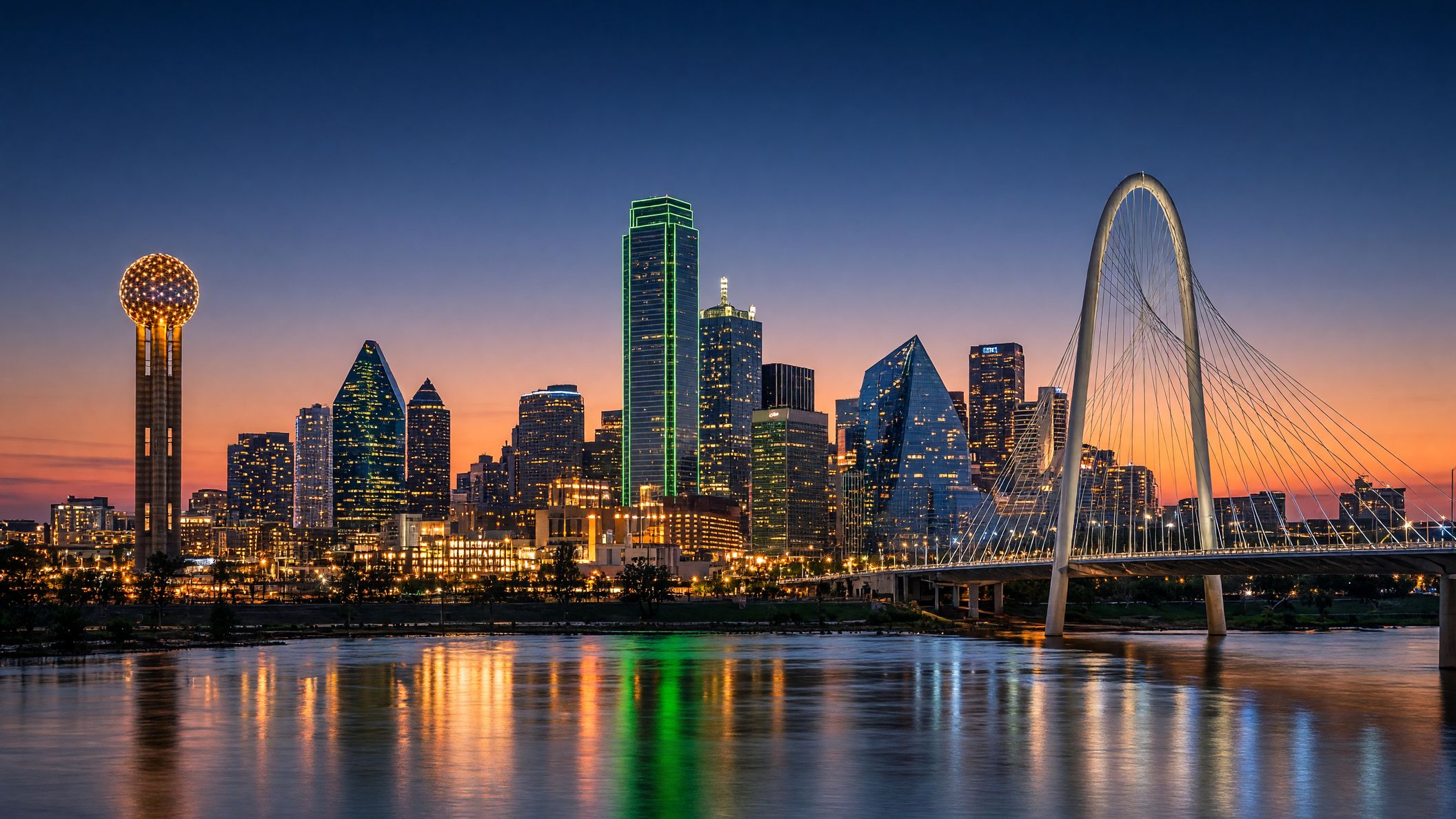 Downtown Dallas skyline at dusk across the Trinity River, with Reunion Tower, the green-lit Bank of America Plaza, Fountain Place and the Margaret Hunt Hill Bridge